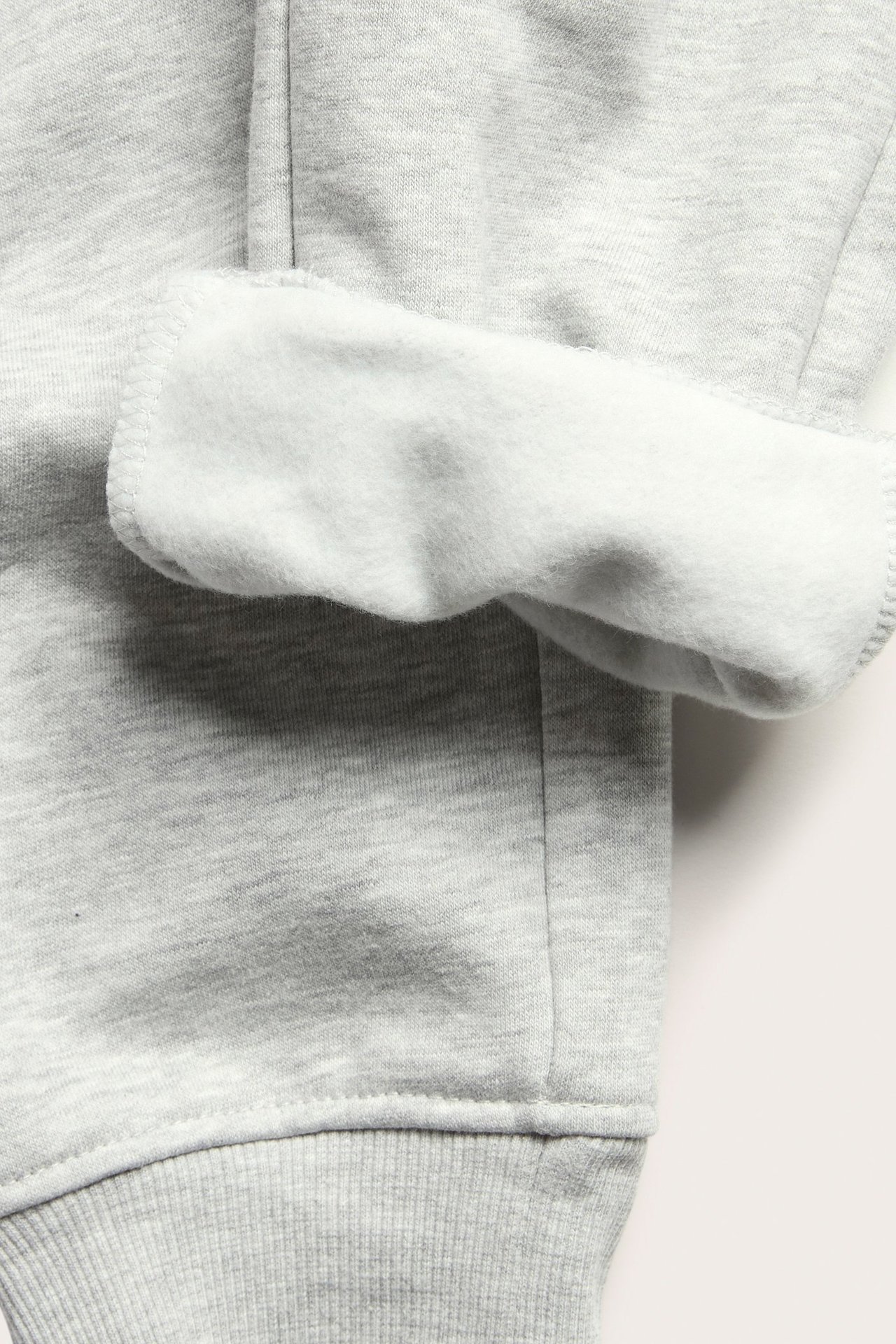 Zbliżenie na szare melanżowe spodnie dresowe z podwiniętym mankietem, ukazujące miękką podszewkę i ściągacz.