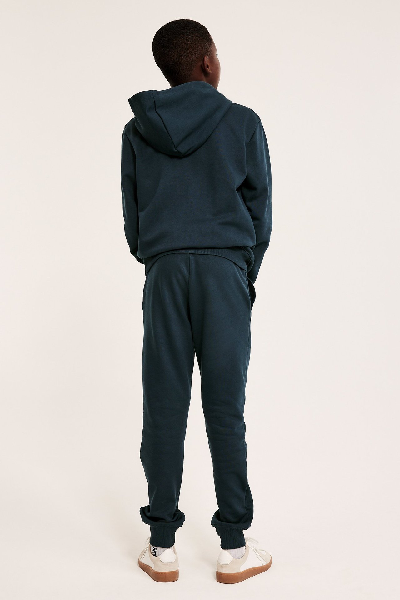 Lapsen takakuva sinisissä puuvillasekoiteverkkarissa, yhteensopivassa hupparissa ja valkoisissa tennareissa.