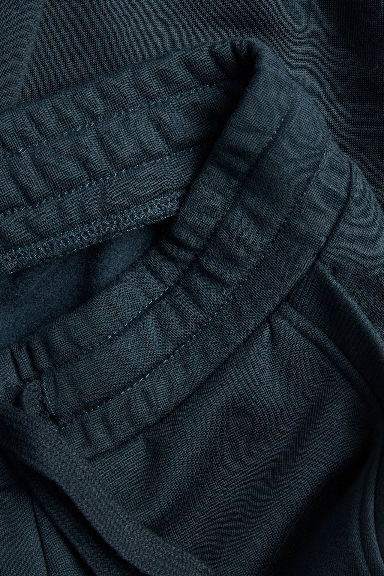 Zbliżenie niebieskich spodni dresowych, pokazujące elastyczny pas z widocznymi szwami i sznurkiem.