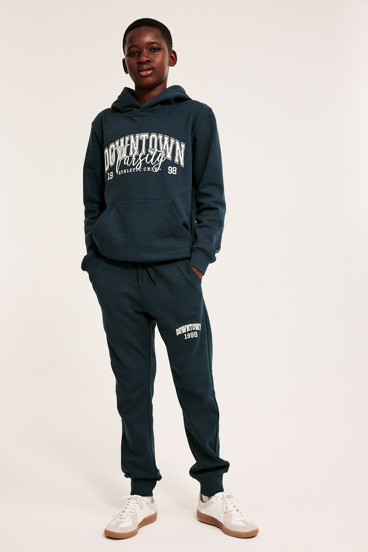 Forfra, et barn iført blå joggebukser med trykk og en matchende blå hettegenser med trykk.