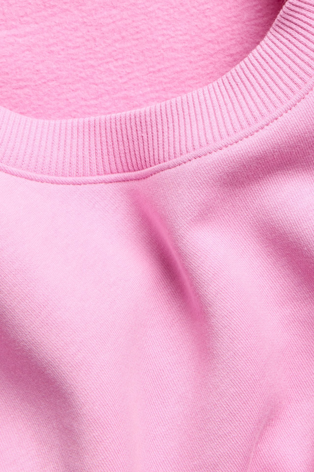 Zbliżenie różowej, gładkiej bluzy z mieszanki bawełny z prążkowanym dekoltem.