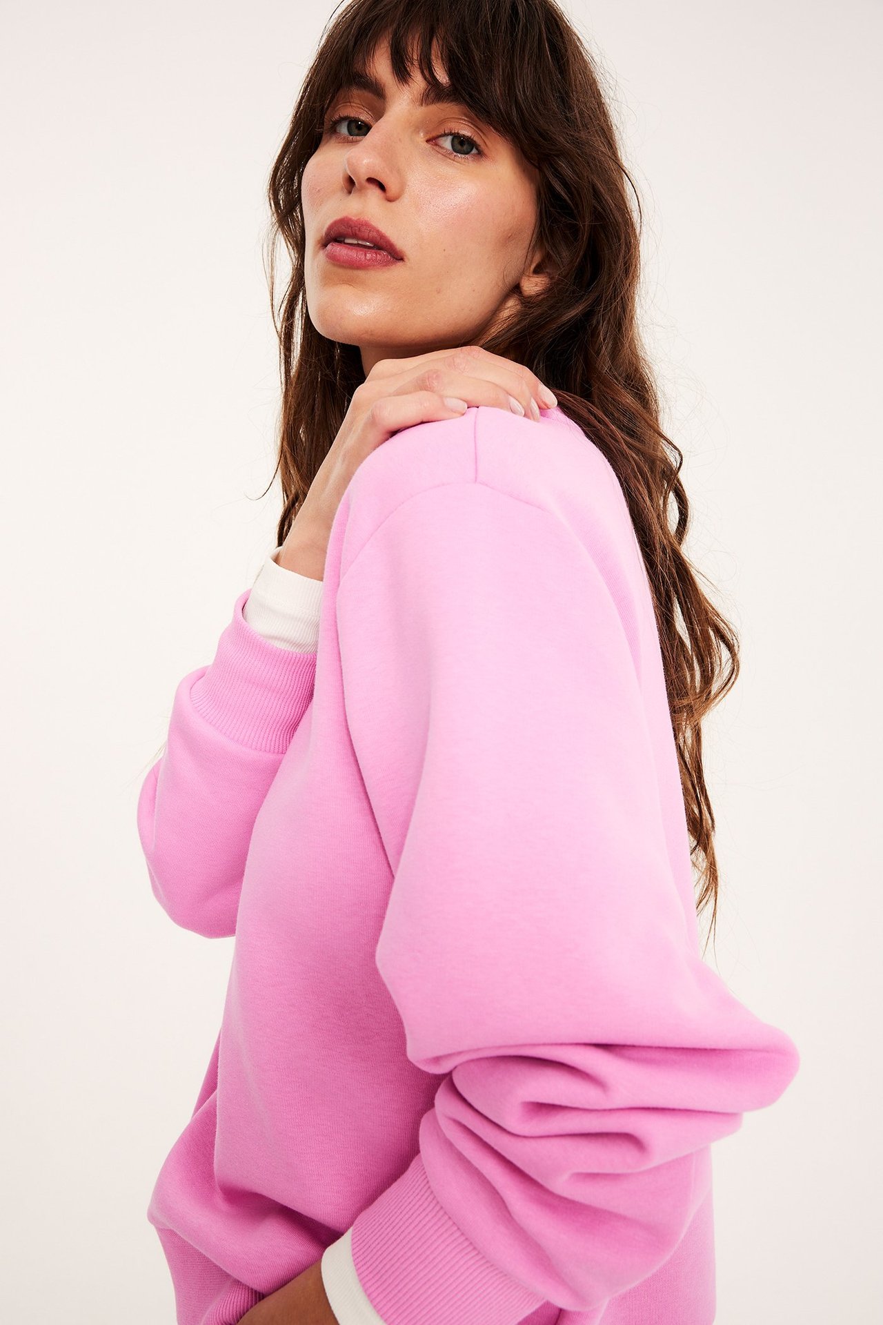 Zbliżenie, widok z boku kobiety w różowej, luźnej bluzie dresowej na białej koszulce z długim rękawem.