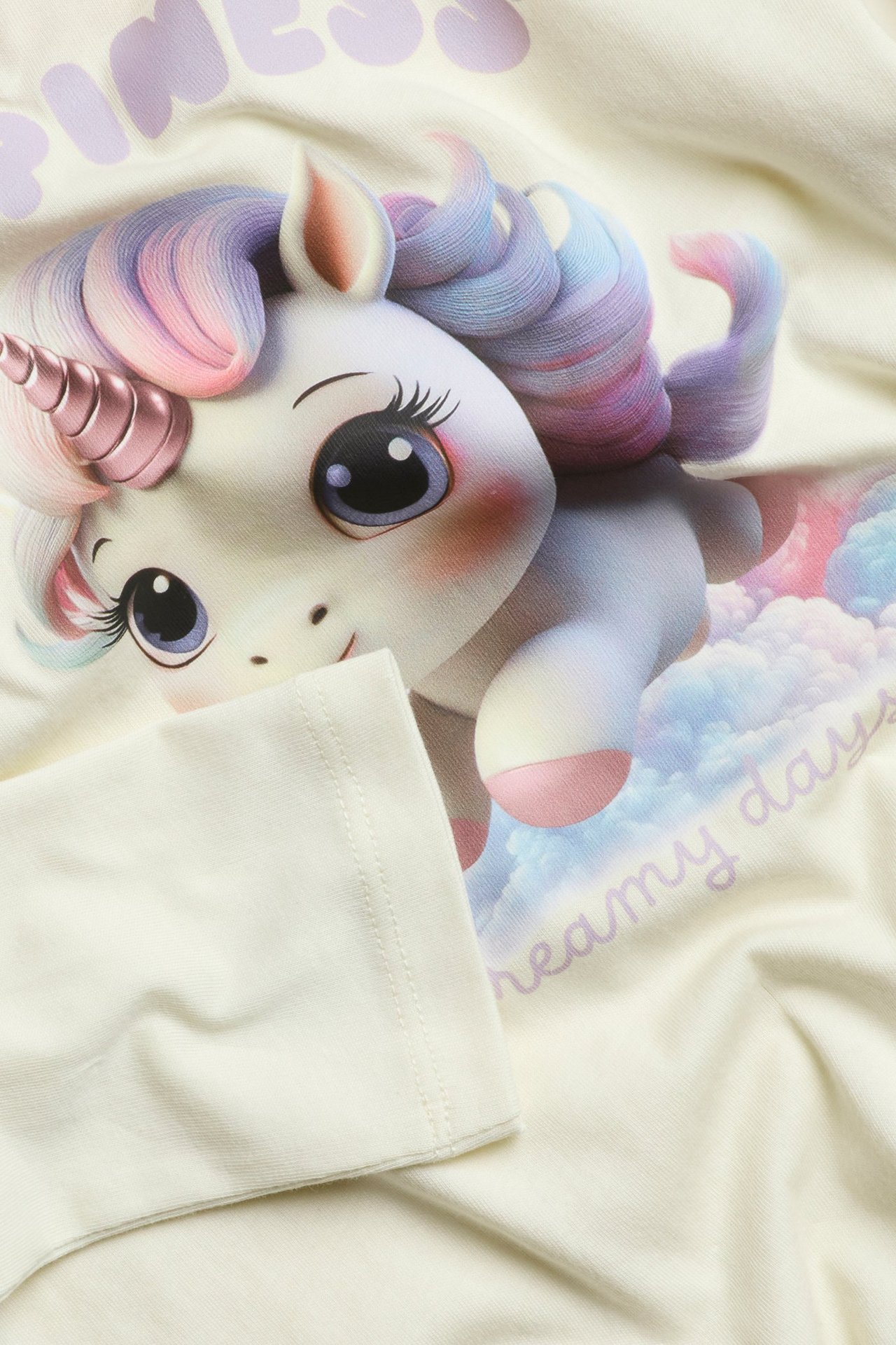 Zbliżenie na białą bawełnianą koszulkę z długim rękawem i uroczym nadrukiem jednorożca z przodu.