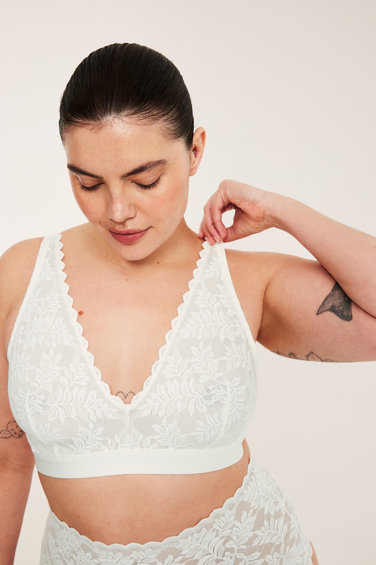 Nainen säätää luonnonvalkoista pitsibralettea, aaltoileva V-pääntie, leveä nauha ja matching alushousut.