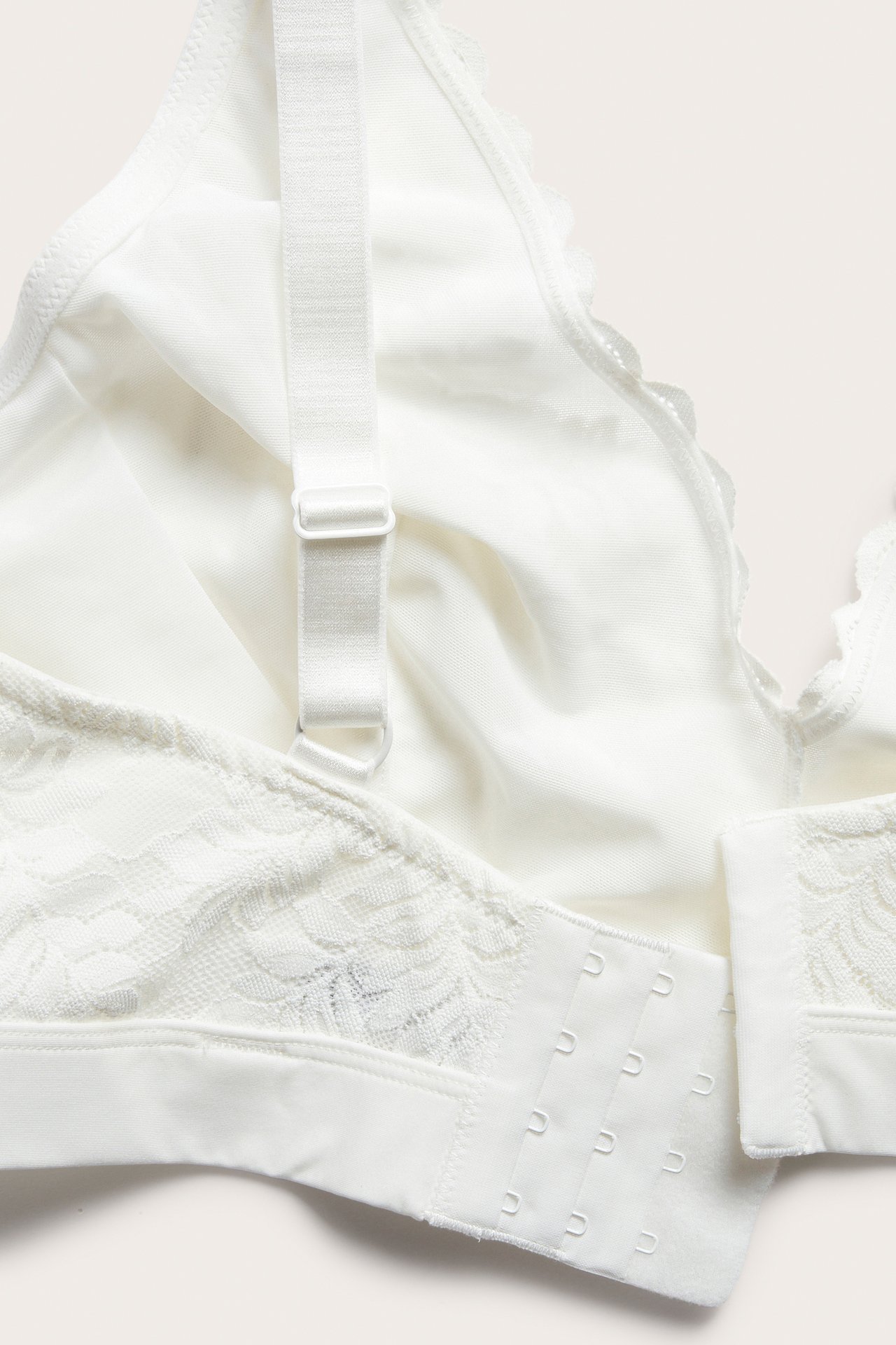 Närbild av en offwhite spets-bralette med justerbart axelband och synlig hakknäppning i ryggen.