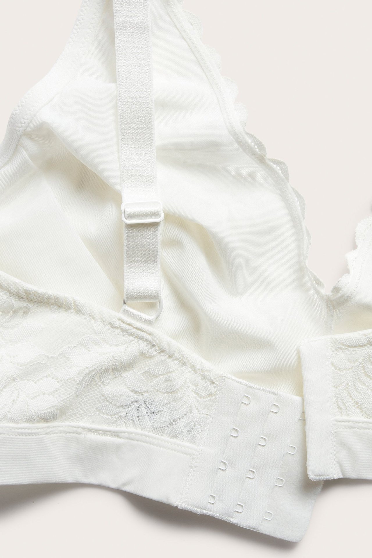Närbild av en offwhite spets-bralette med justerbart axelband och synlig hakknäppning i ryggen.