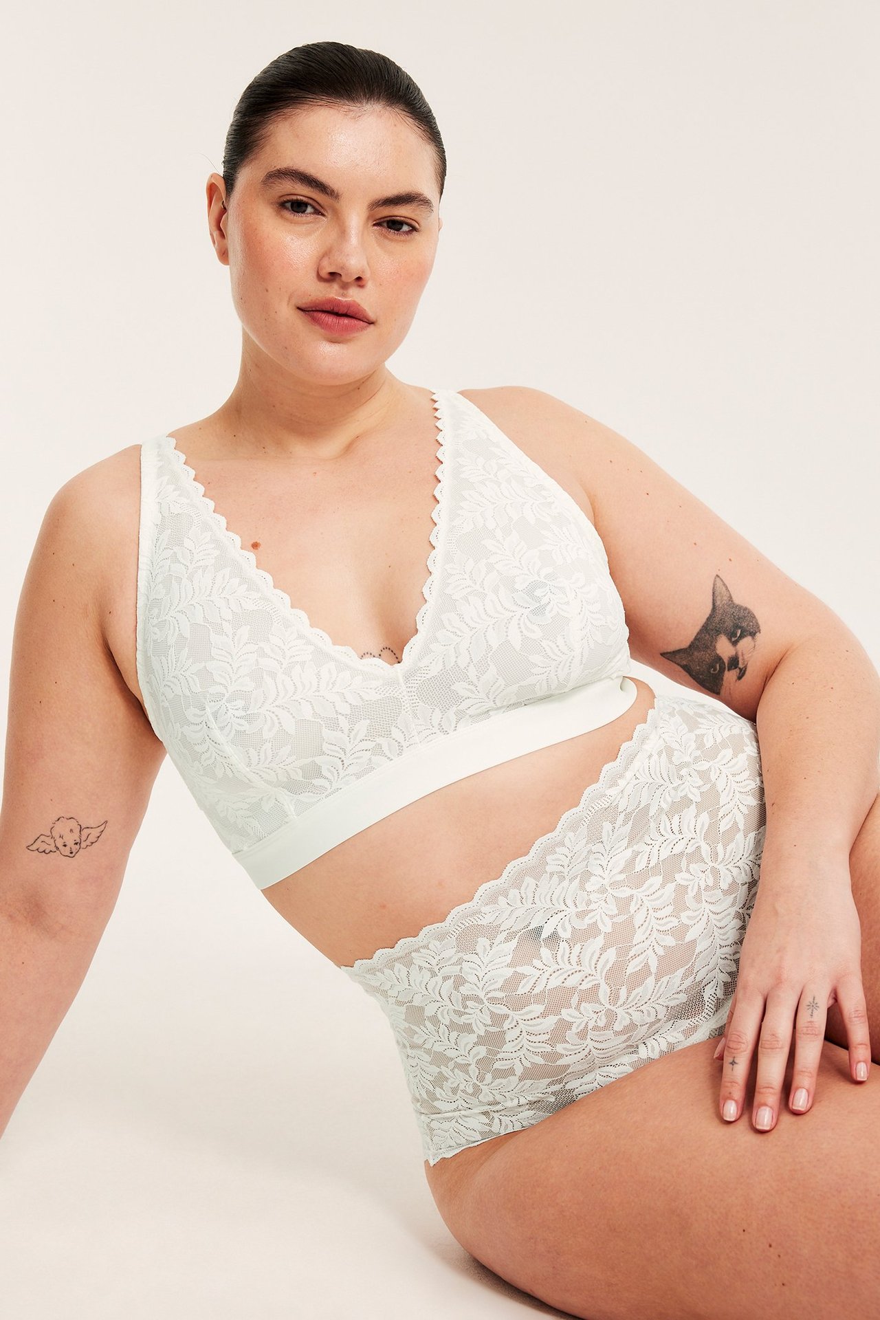 Framsida av en kvinna i en mjuk off-white spetsbralette och matchande höga spetstrosor.
