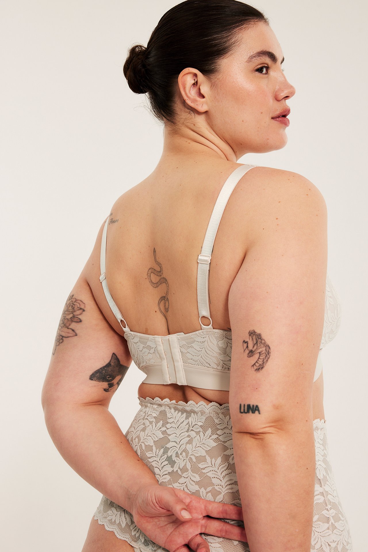 Bakåtvänd bild av en kvinna i ljusbeige spets-bralette med justerbara band och matchande höga spetstrosor.