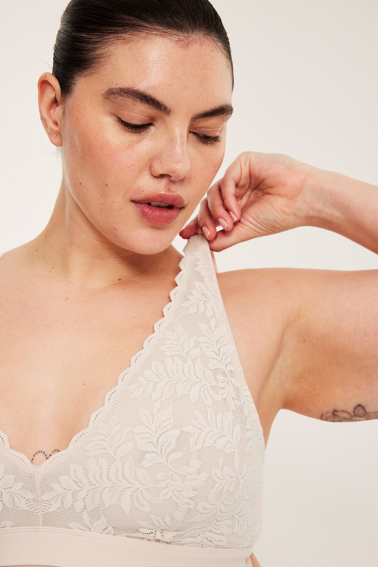 Lähikuva naisesta, yllään vaaleanpunainen kukkakuvioinen pitsibralette, pitäen olkainta.