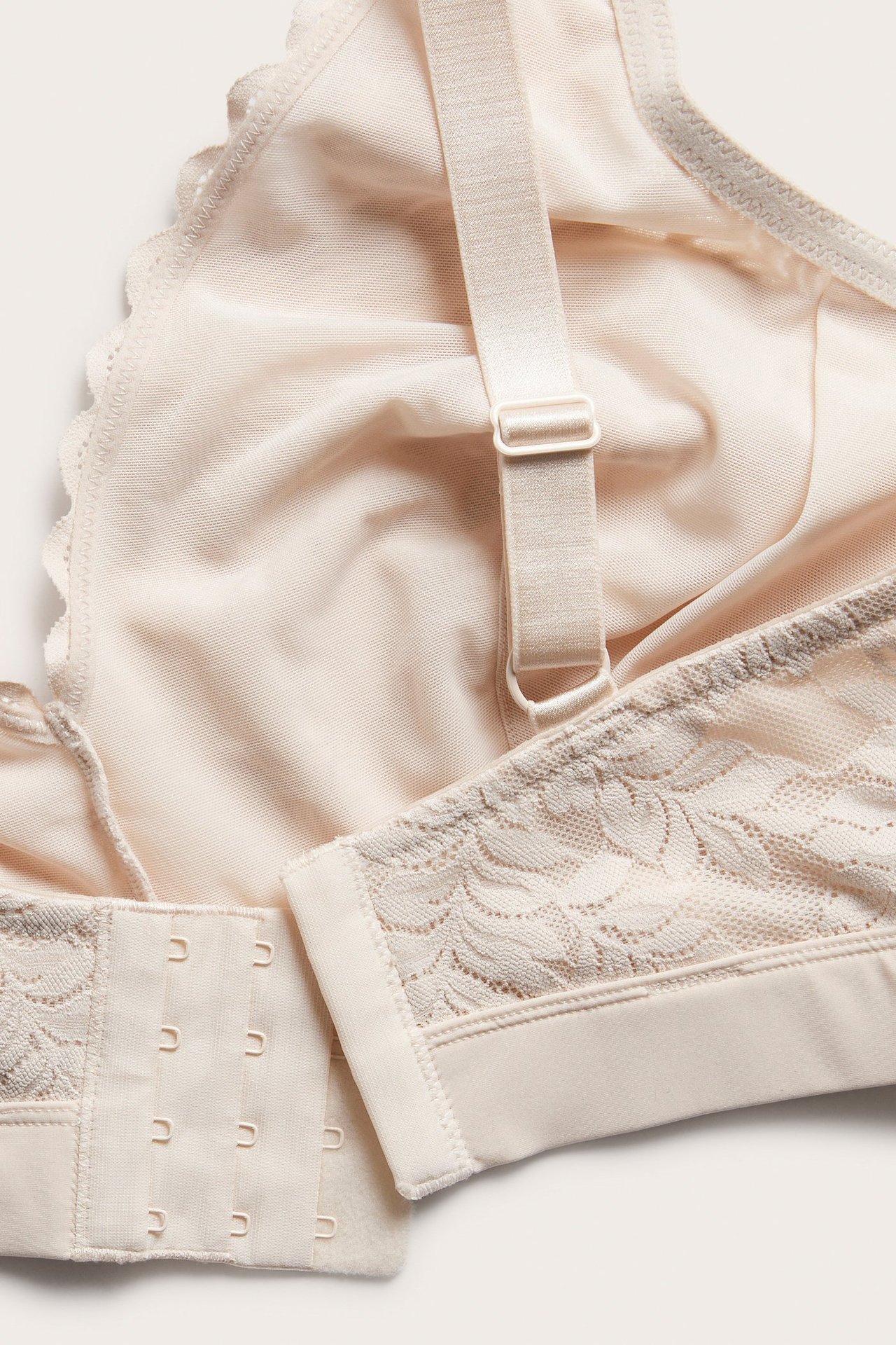 Närbild uppifrån på en ljusrosa spets-bralette med hyskknäppning och justerbara axelband.