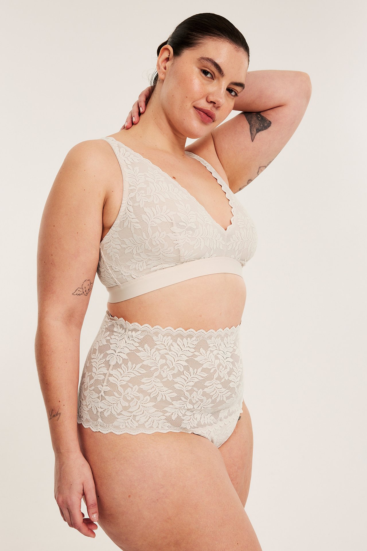 Framifrån: kvinna i ljusrosa spetsbralette och matchande högmidjade spetstrosor.