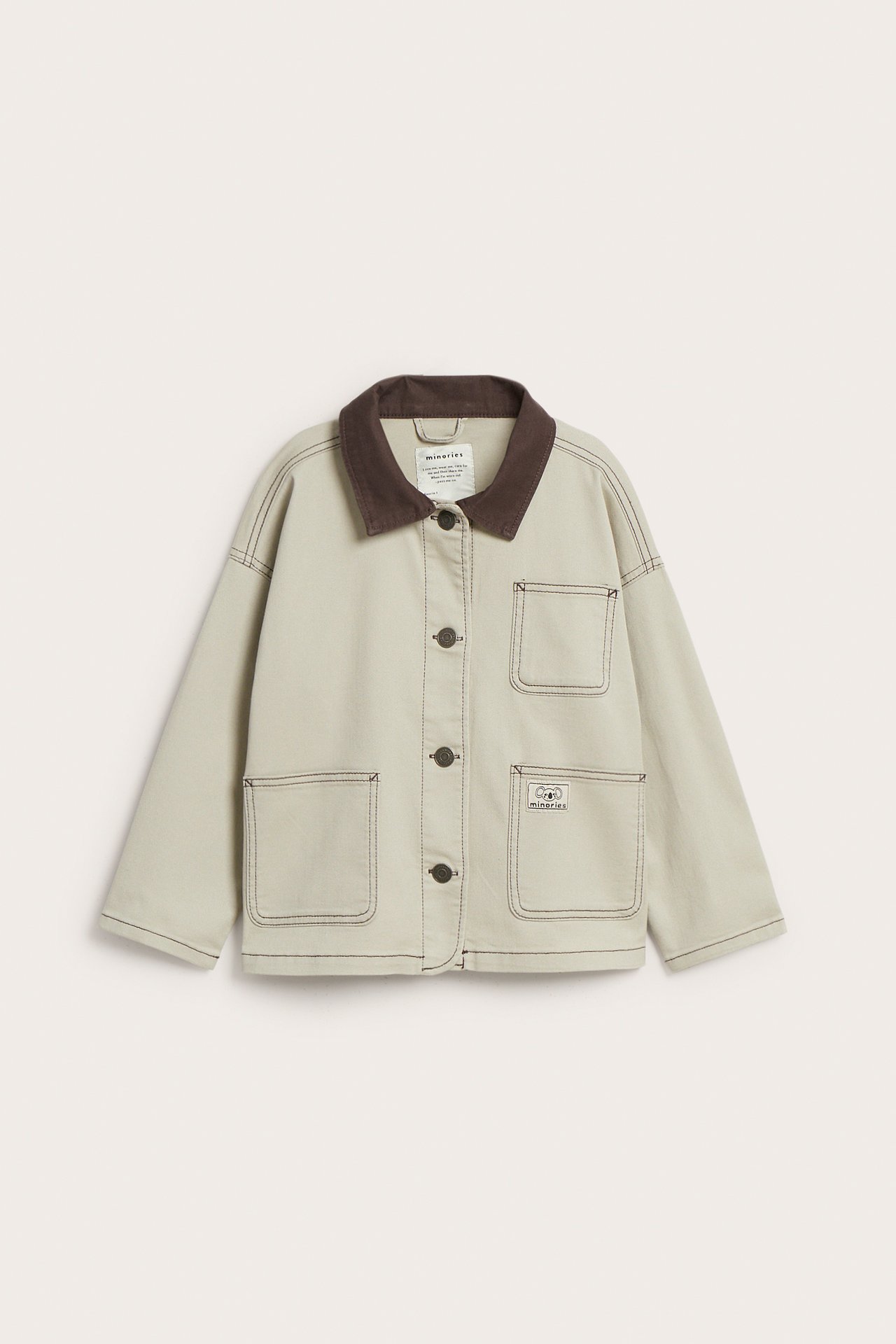 Framifrån: Beige bomullstwilljacka med mörkbrun krage, knappstängning och fyra framfickor.