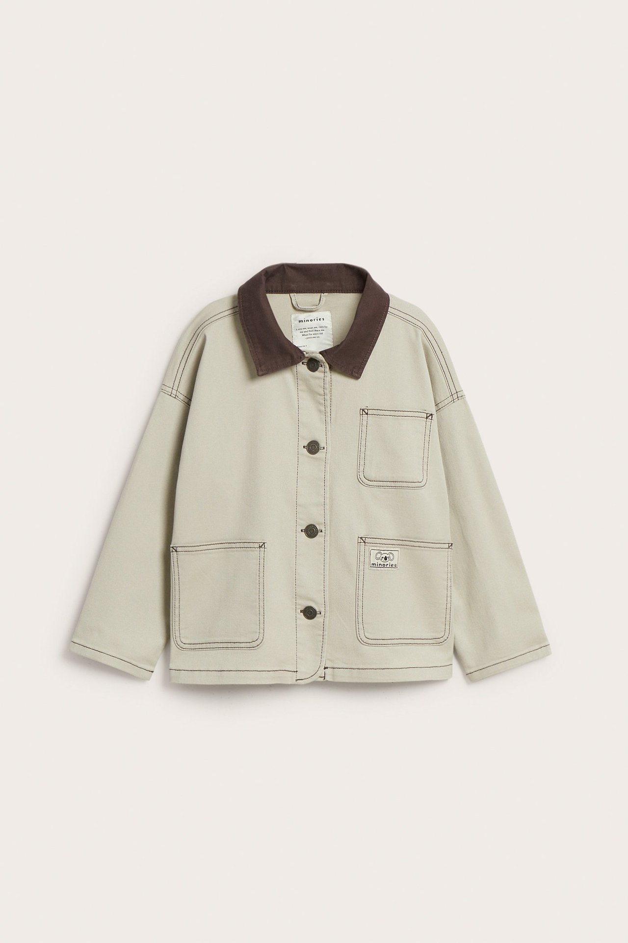 Edestä: Beige puuvillatvillitakki tummanruskealla kauluksella, nappikiinnityksellä ja neljällä etutaskulla.