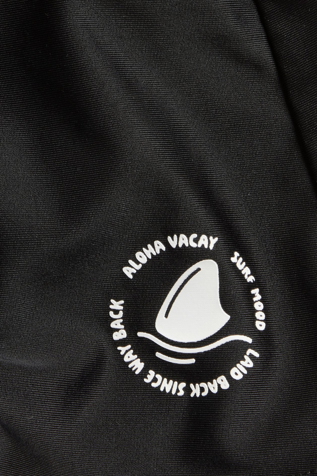 Lasten mustien uimahousujen lähikuva, jossa valkoinen pyöreä haineväkuvio ja teksti.