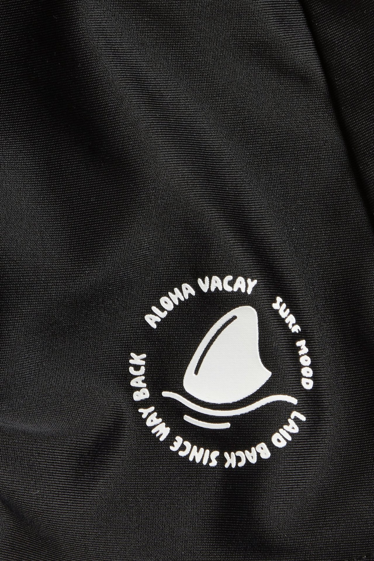 Lasten mustien uimahousujen lähikuva, jossa valkoinen pyöreä haineväkuvio ja teksti.