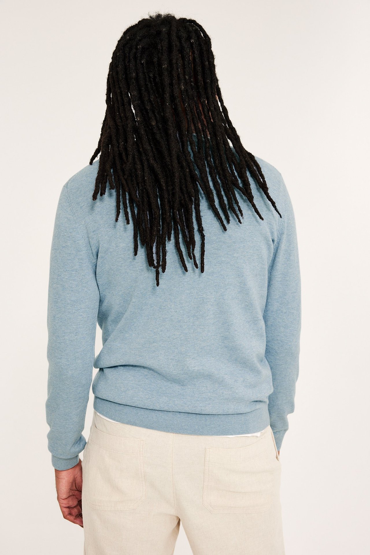 Mężczyzna z tyłu w jasnoniebieskim melanżowym, cienkim swetrze bawełnianym i jasnobeżowych spodniach.