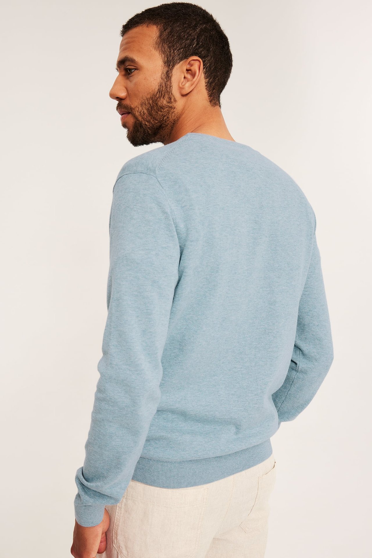 Sidovy av en man i en ljusblå melerad finstickad bomullströja och beige byxor.