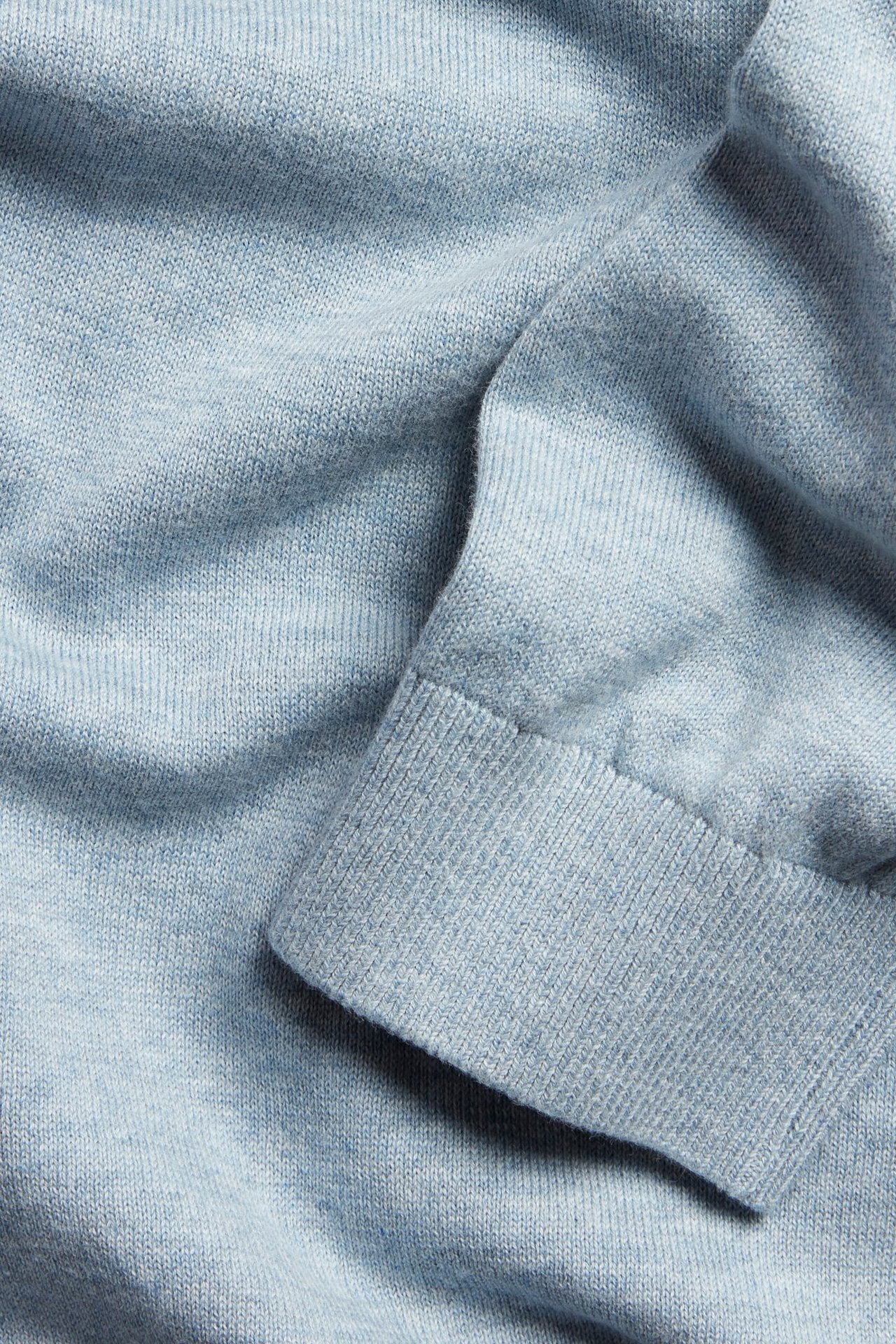 Närbild på en ljusblå melerad finstickad tröja i 100% bomull med ribbad mudd.