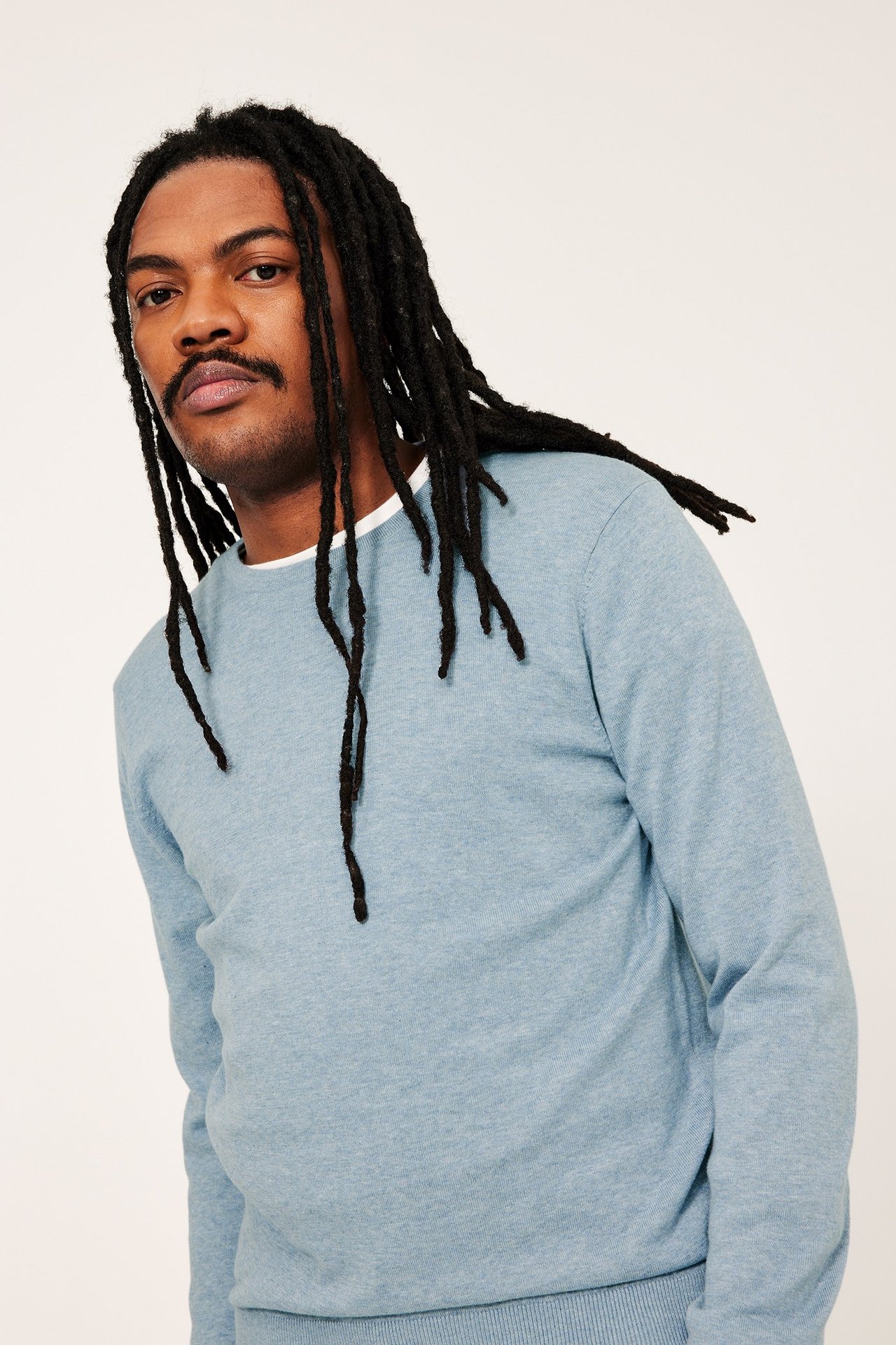Mężczyzna przodem w jasnoniebieskim, melanżowym swetrze bawełnianym na białym T-shircie.