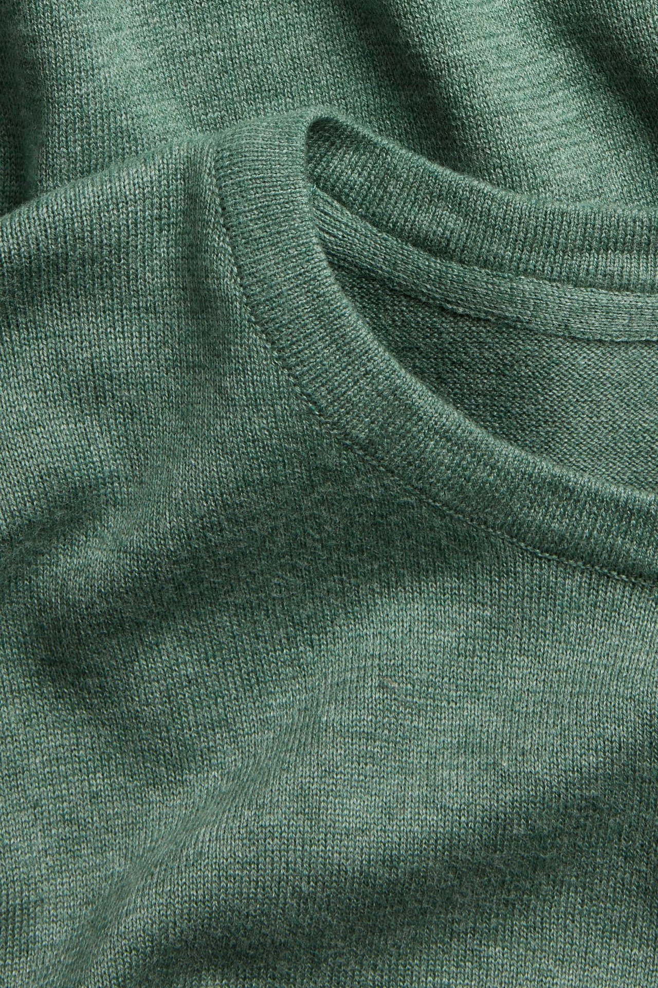 Zbliżenie na zielony melanżowy sweter z cienkiej dzianiny bawełnianej z okrągłym dekoltem.