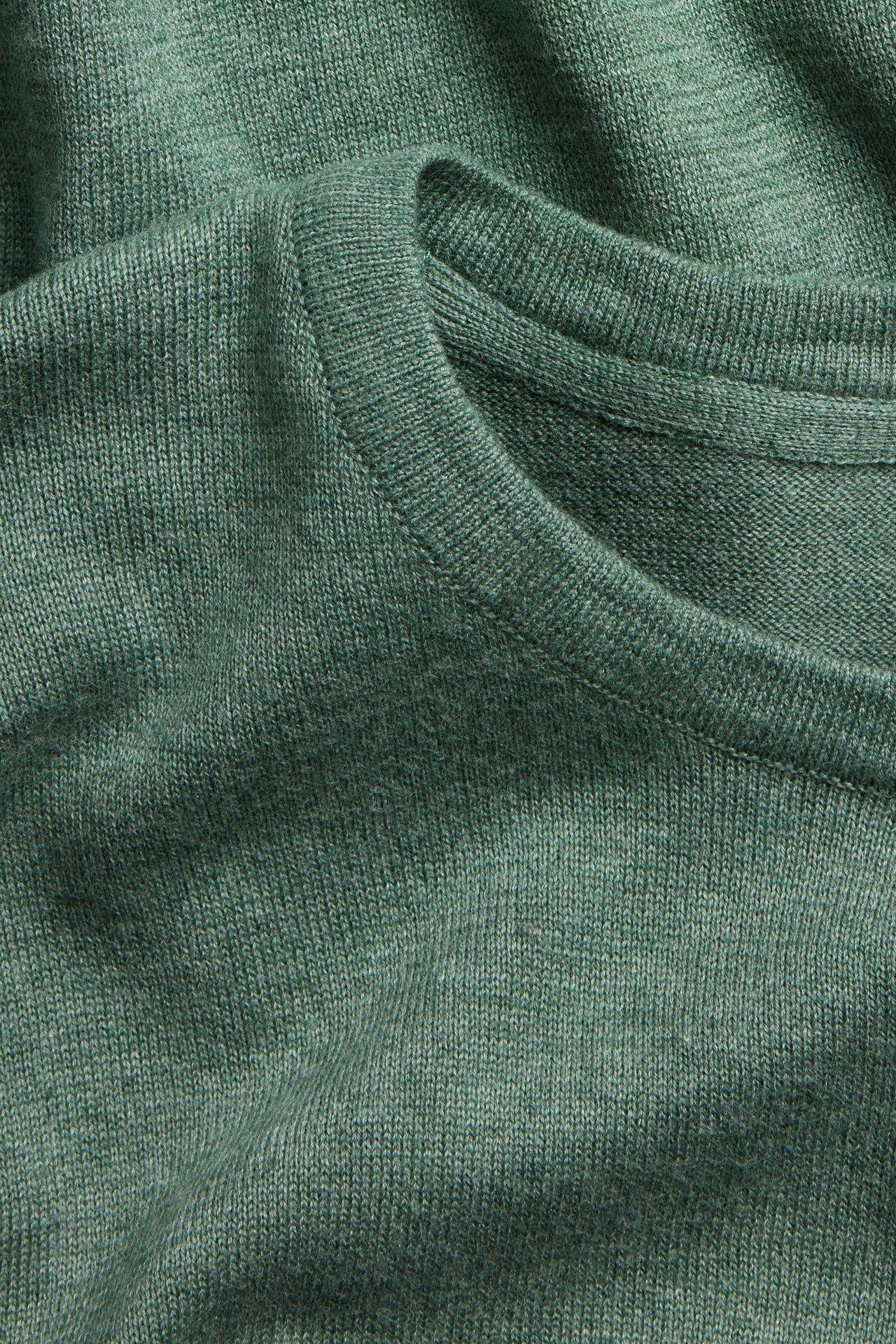 Närbild på en grönmelerad finstickad bomullströja med rund halsringning.