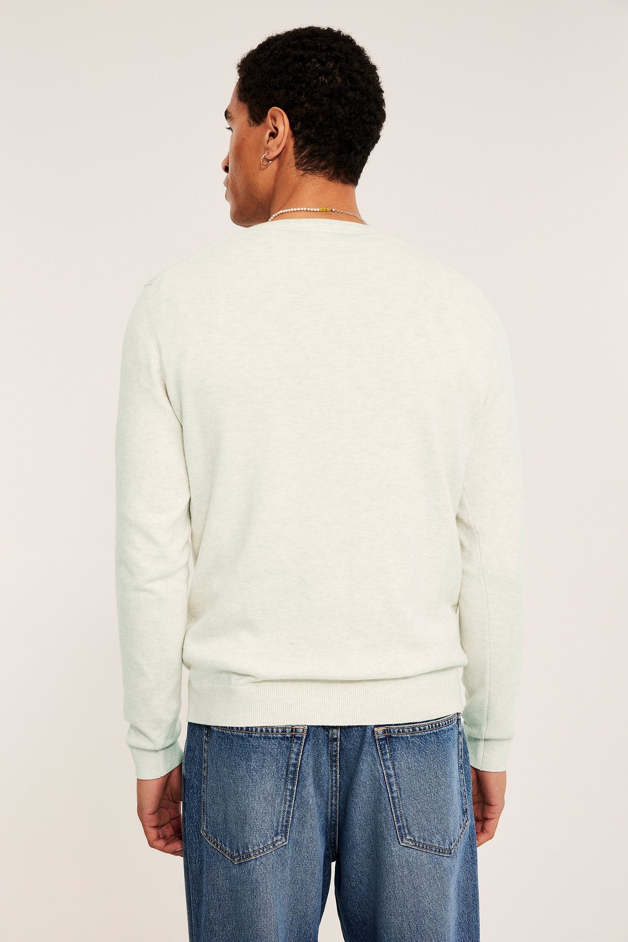 Bakfra av en mann i en lysmelert finstrikket bomullsgenser og blå denimjeans.