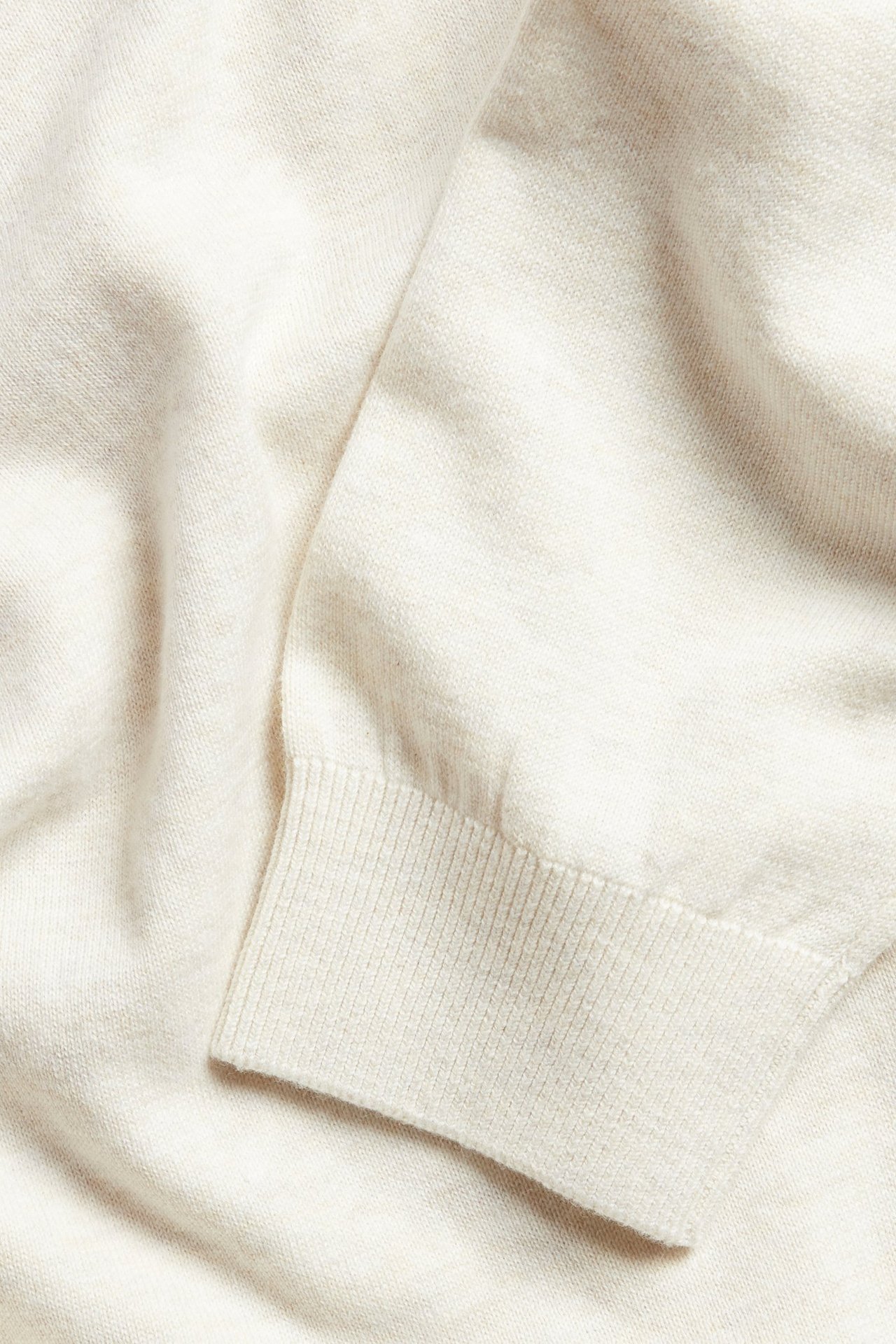 Närbild av en melerad vit finstickad bomullströja med ribbad mudd.