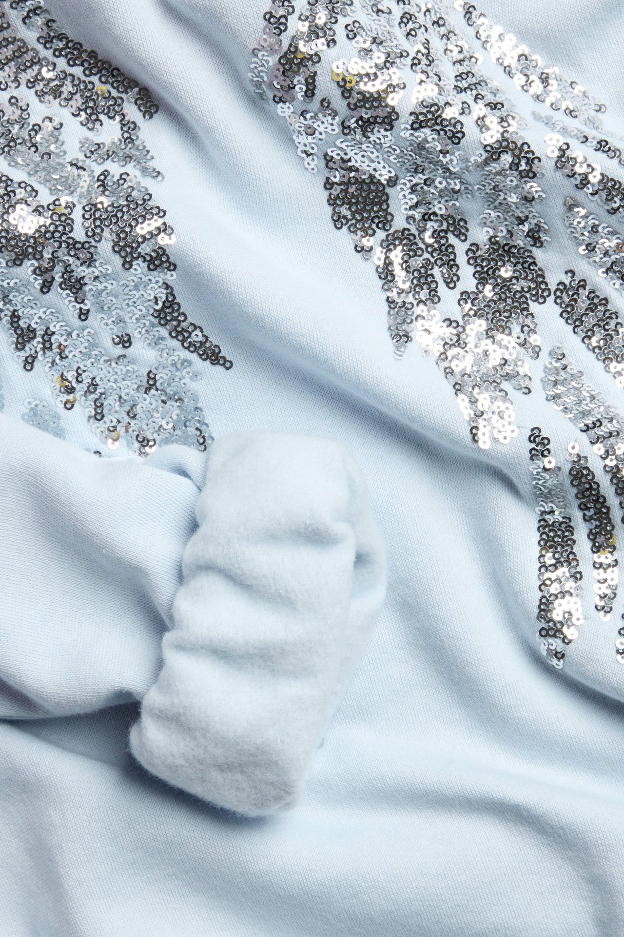Zbliżenie jasnoniebieskiej bluzy z błyszczącymi srebrnymi aplikacjami skrzydeł z cekinów.