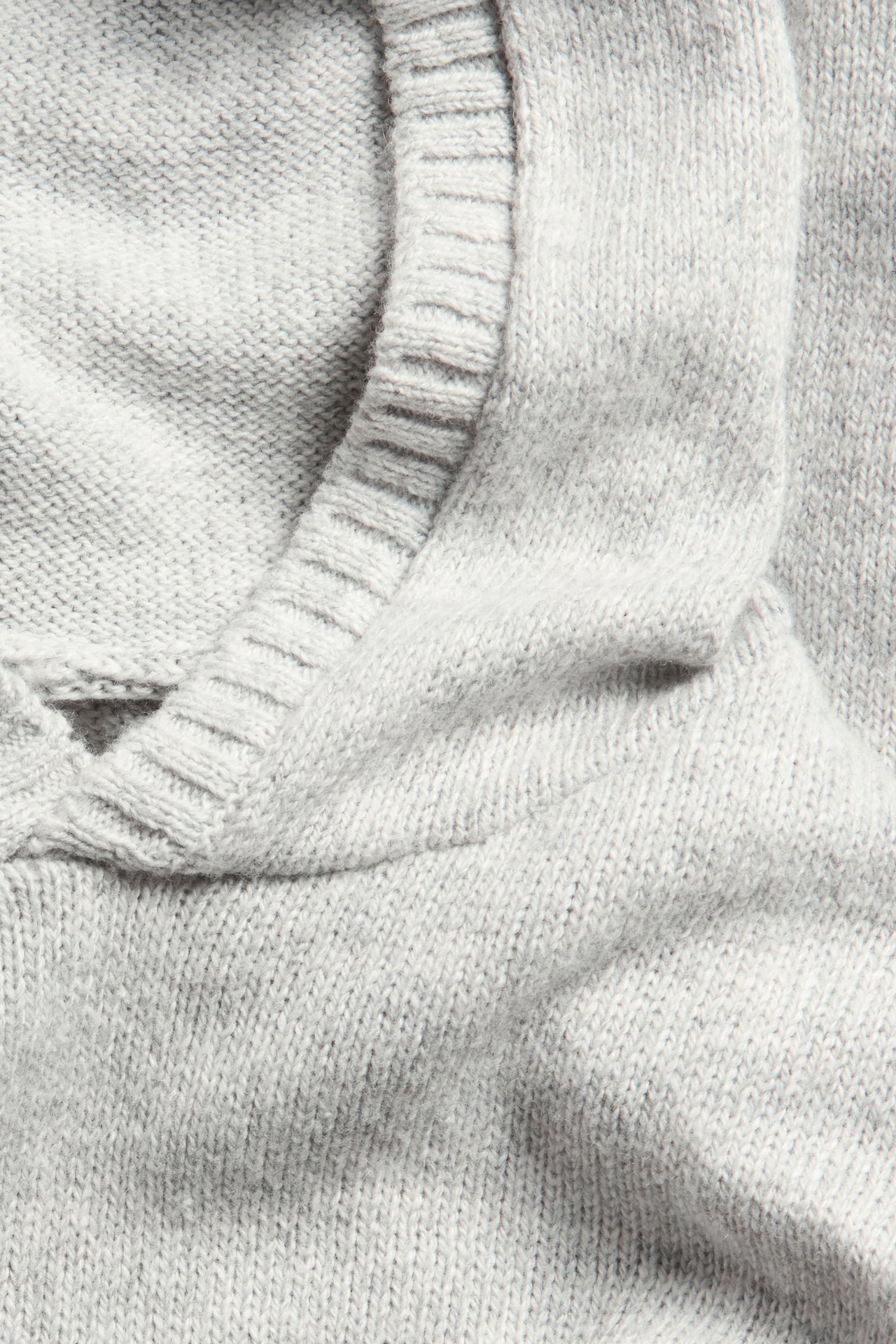 Nærbilde av en lys grå strikket hoodie, som viser det myke stoffet og hetteåpningen.