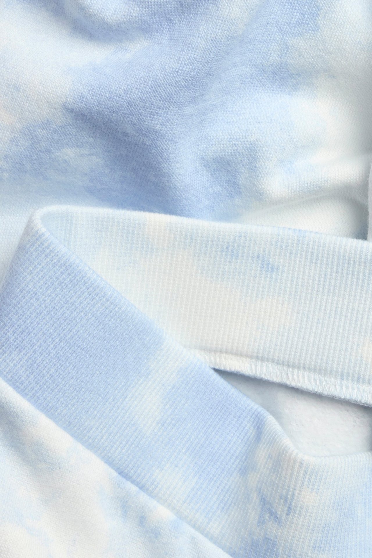 Zbliżenie na jasnoniebieskie i białe spodnie dresowe tie-dye z prążkowanym pasem.