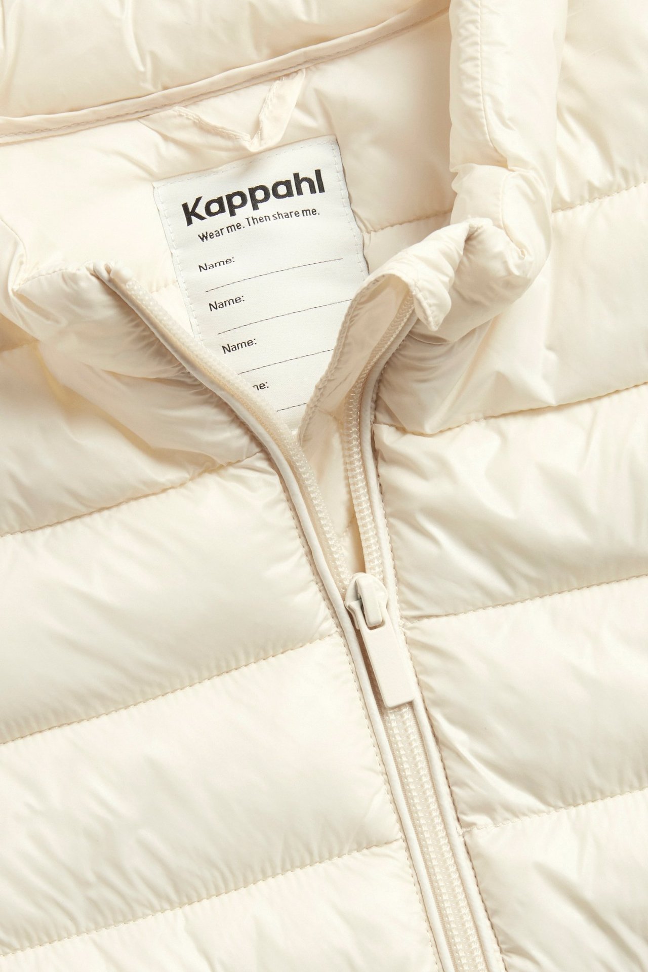 Lähikuva luonnonvalkoisesta kiiltävästä topatusta kevyttoppatakista, jossa on vetoketju ja sisäetiketti.