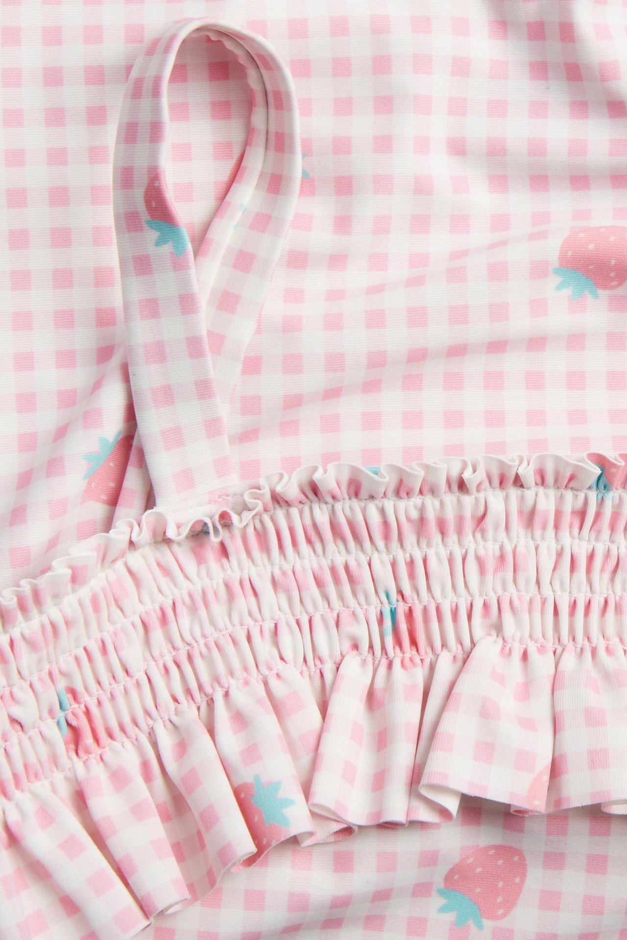 Zbliżenie różowego, kraciastego dziecięcego stroju kąpielowego z truskawkami, marszczeniem, falbaną i ramiączkiem.