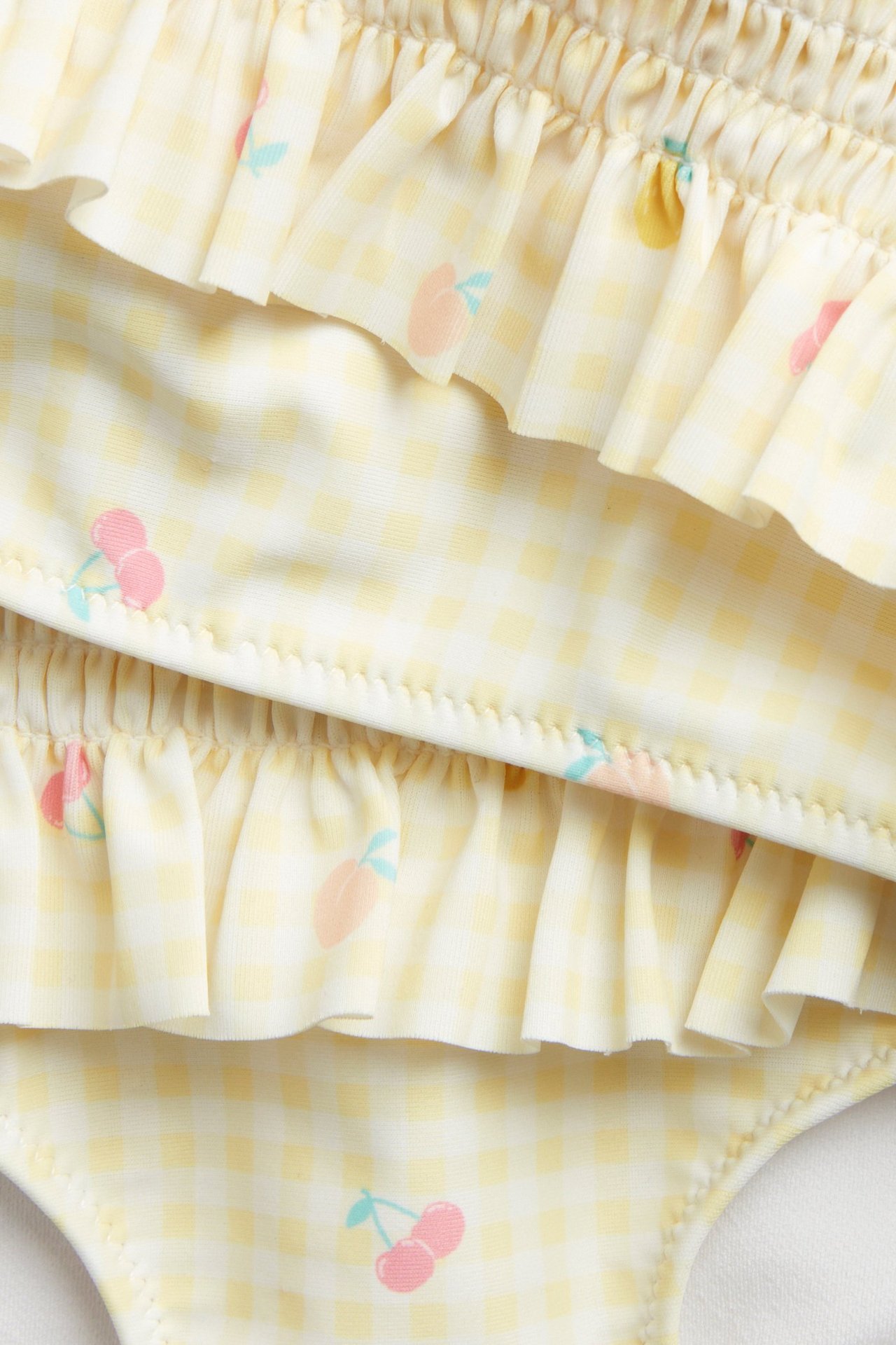 Zbliżenie na dziecięce żółte bikini w kratkę ze ściągaczem, falbankami i owocowym wzorem.