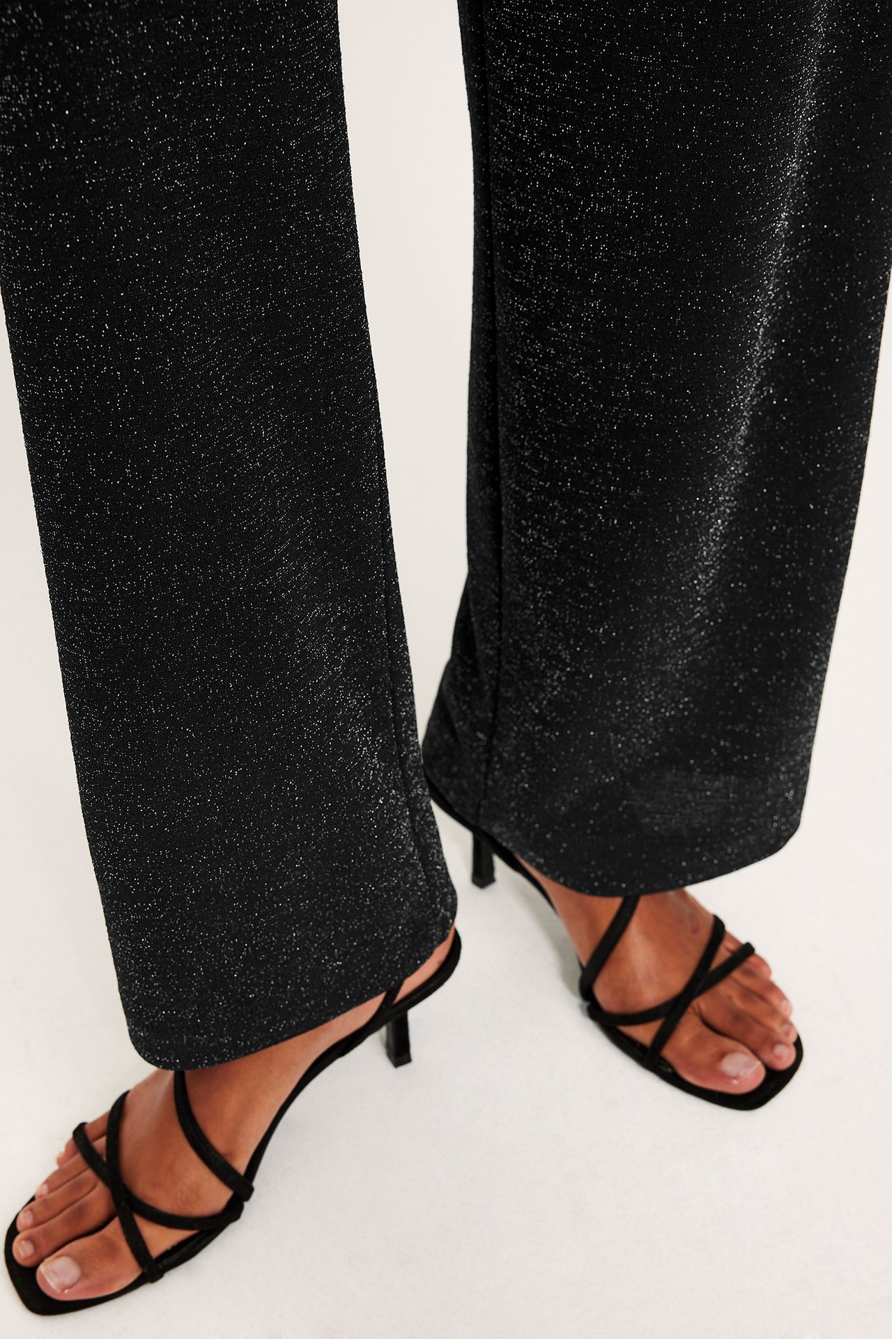 Kvinnlig modell i svarta glitterkostymbyxor med vida ben, över svarta high heels.