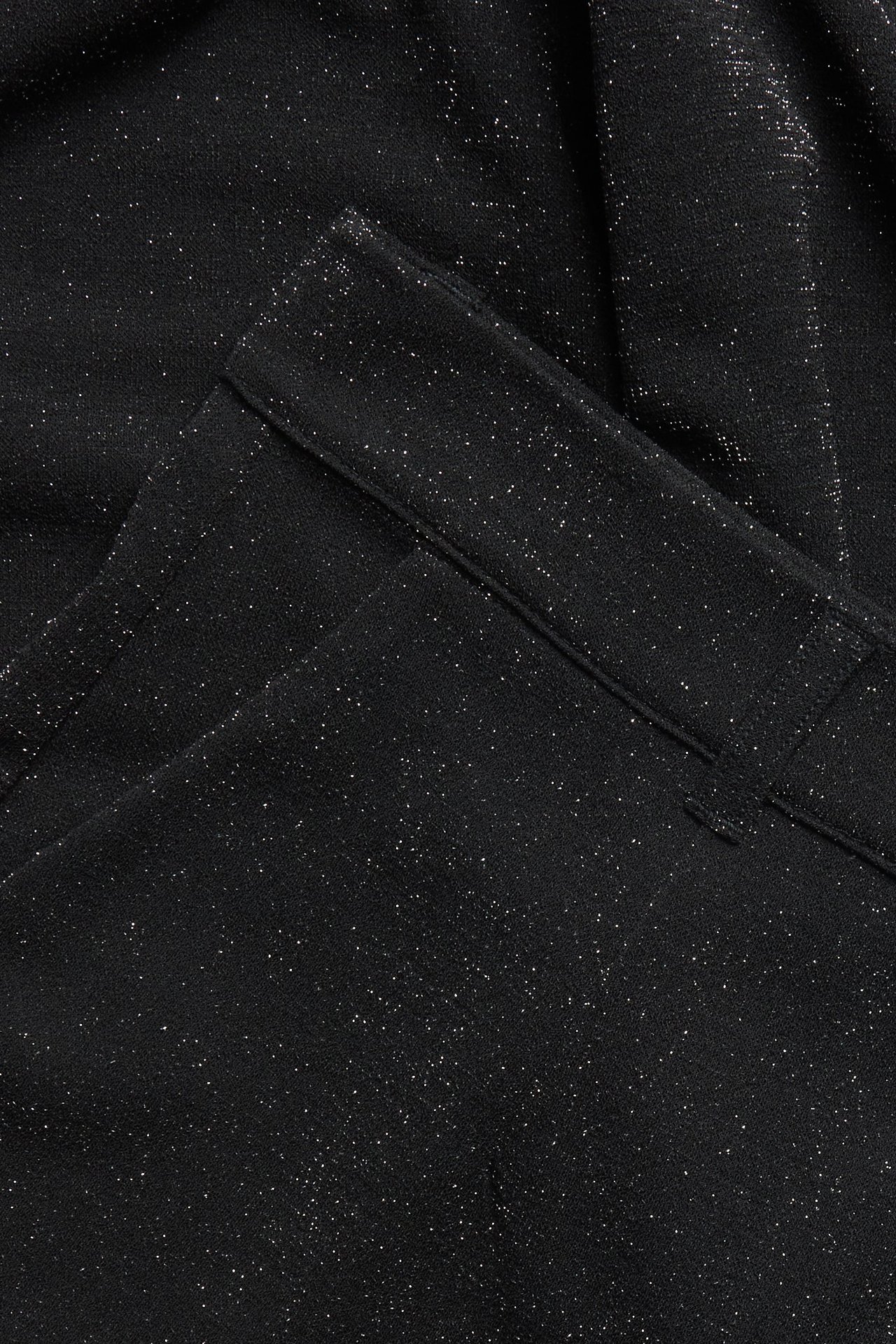 Nærbilde av svarte dressbukser i punto jersey med glitter og lurexdetaljer.