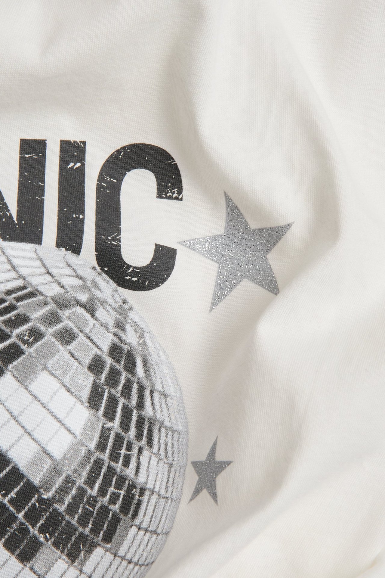 Zbliżenie: Ecru bawełniana koszulka z nadrukiem kuli dyskotekowej i brokatowych srebrnych gwiazd z przodu.