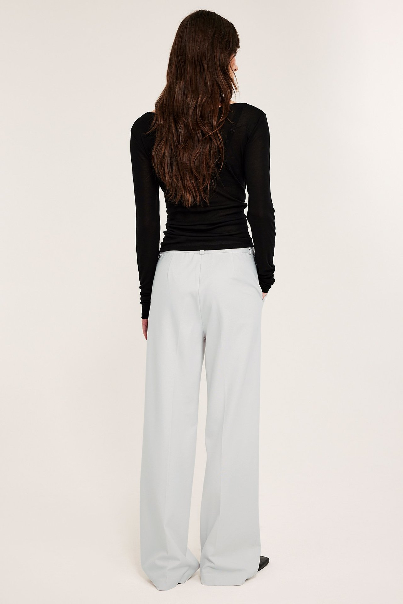 Widok z tyłu: kobieta w ecru, szerokich spodniach garniturowych z gumką i czarnej bluzce z długim rękawem.
