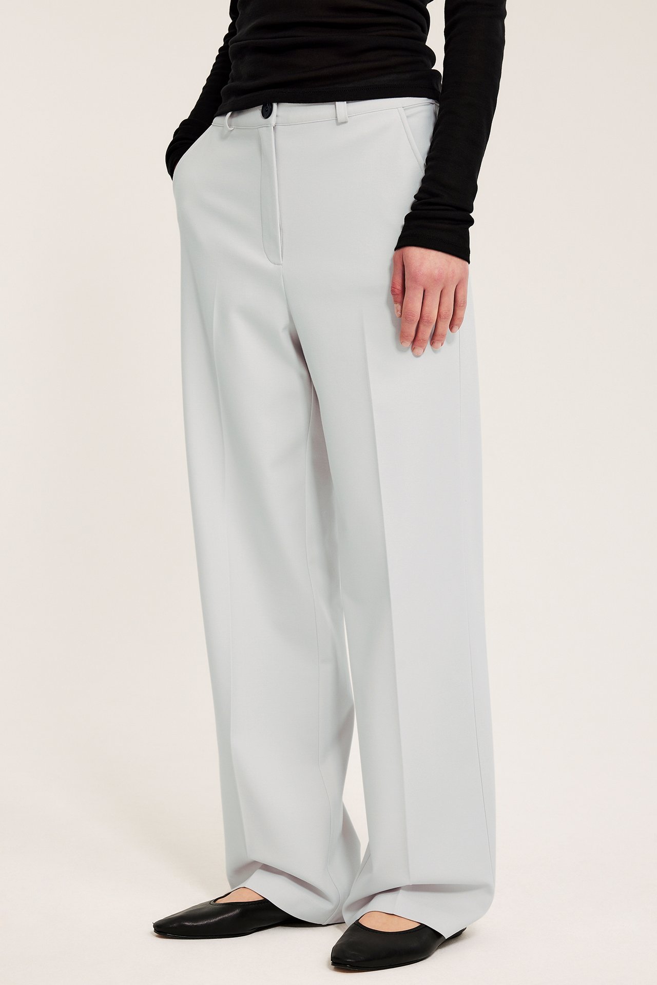 Sidebilde av en kvinne i hvite vide dressbukser, stylet med en svart langermet topp og svarte flate sko.