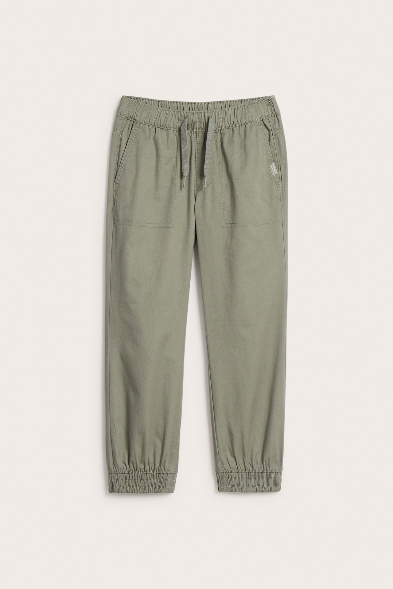 Frontvy: Khakigröna vävda bomullsbyxor för barn med resårmidja, dragsko och resårmuddar.