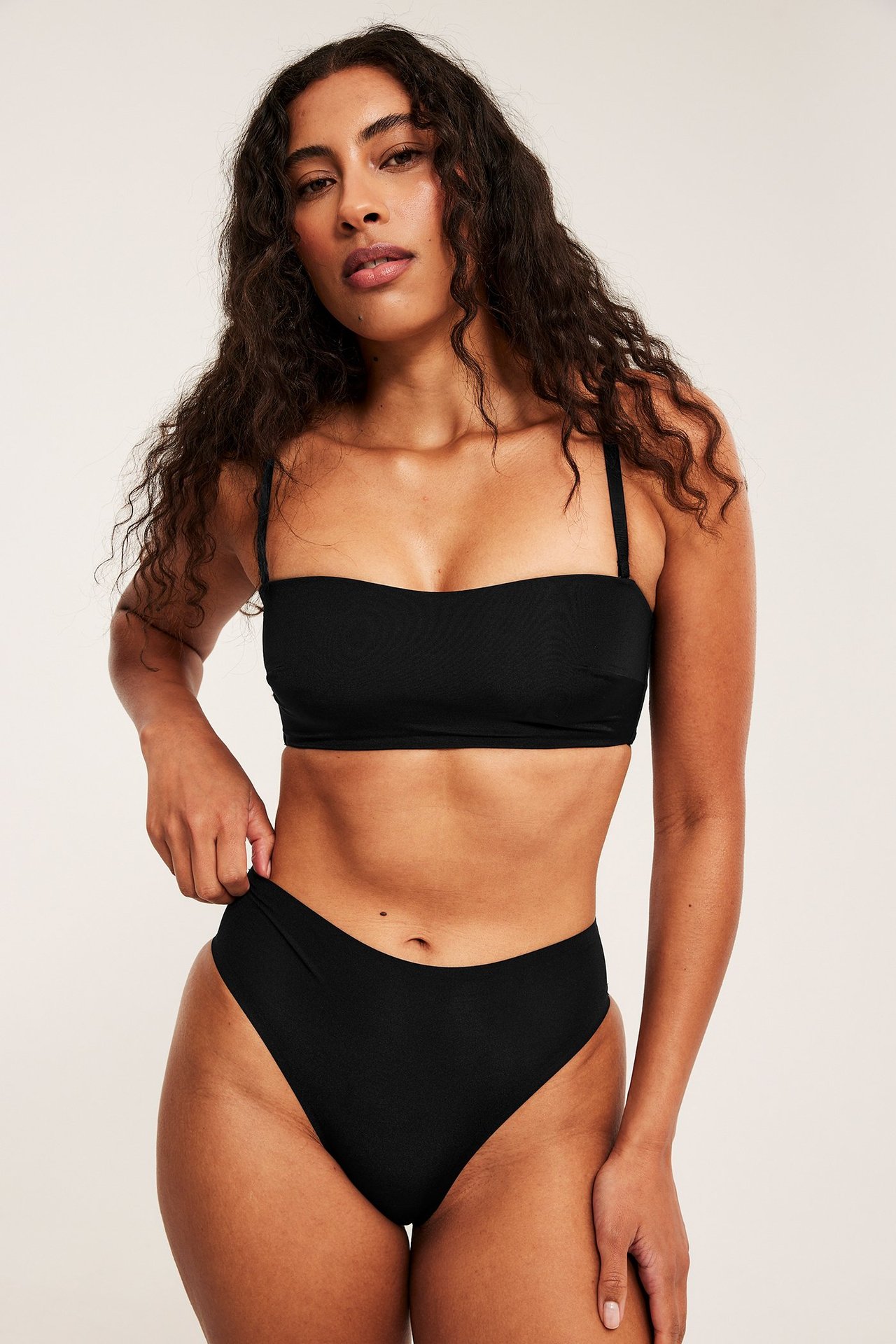 Frontbilde av en kvinne i svart bandeau-BH med tynne stropper og matchende høytlivstruser.
