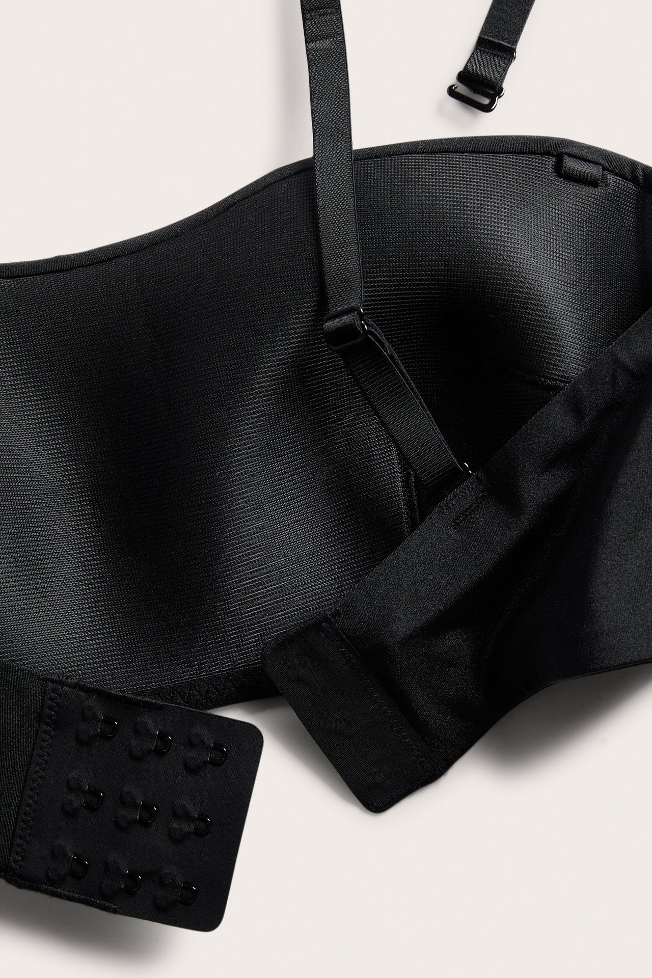 Nærbilde av en svart polstret bandeau-BH med avtakbare skulderstropper og hektefeste.