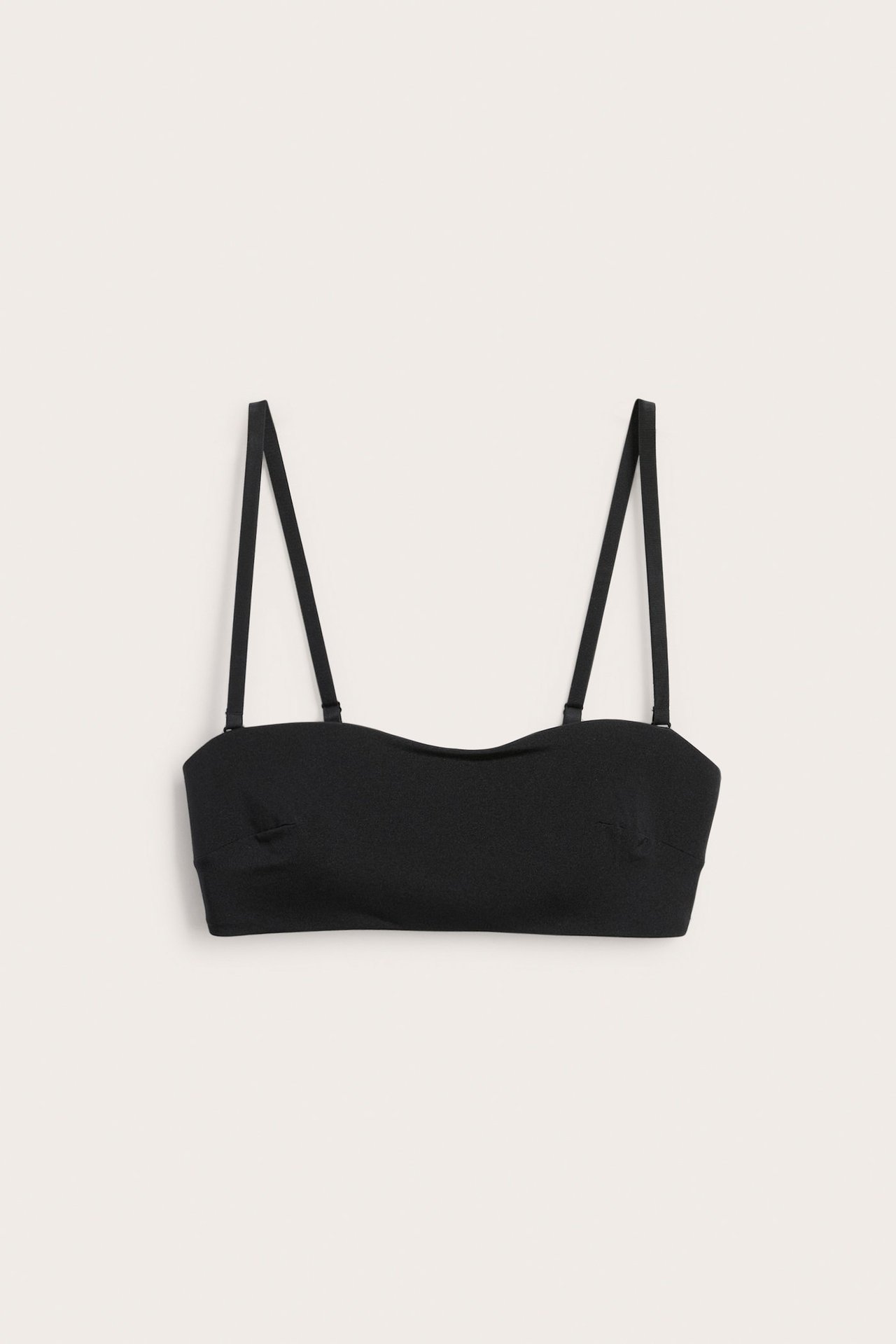 Forfra, en svart mykt polstret bandeau-BH med justerbare, avtakbare stropper.
