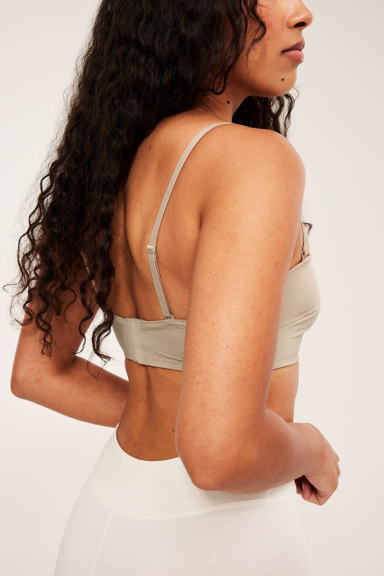 Sida-bakifrån vy av en kvinna i en beige vadderad bandeau-bh med justerbara axelband och vita underdelar.