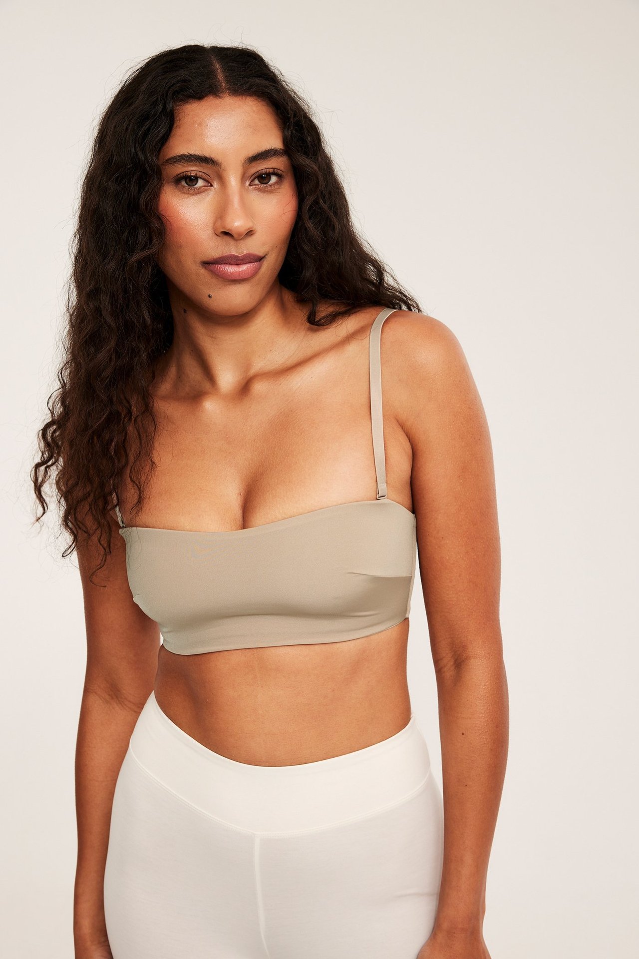 Forfra av en kvinne i brun polstret bandeau-BH med avtagbar stropp og hvit underdel.