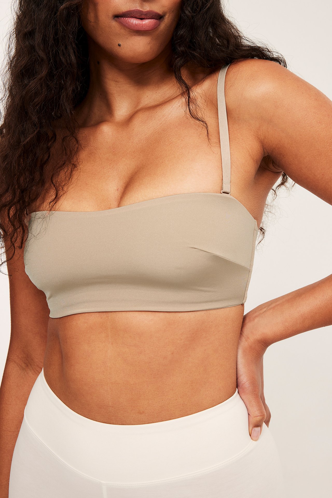 Nærbilde, forfra, av kvinne i beige polstret bandeau-BH med avtakbar stropp og hvite underdeler.