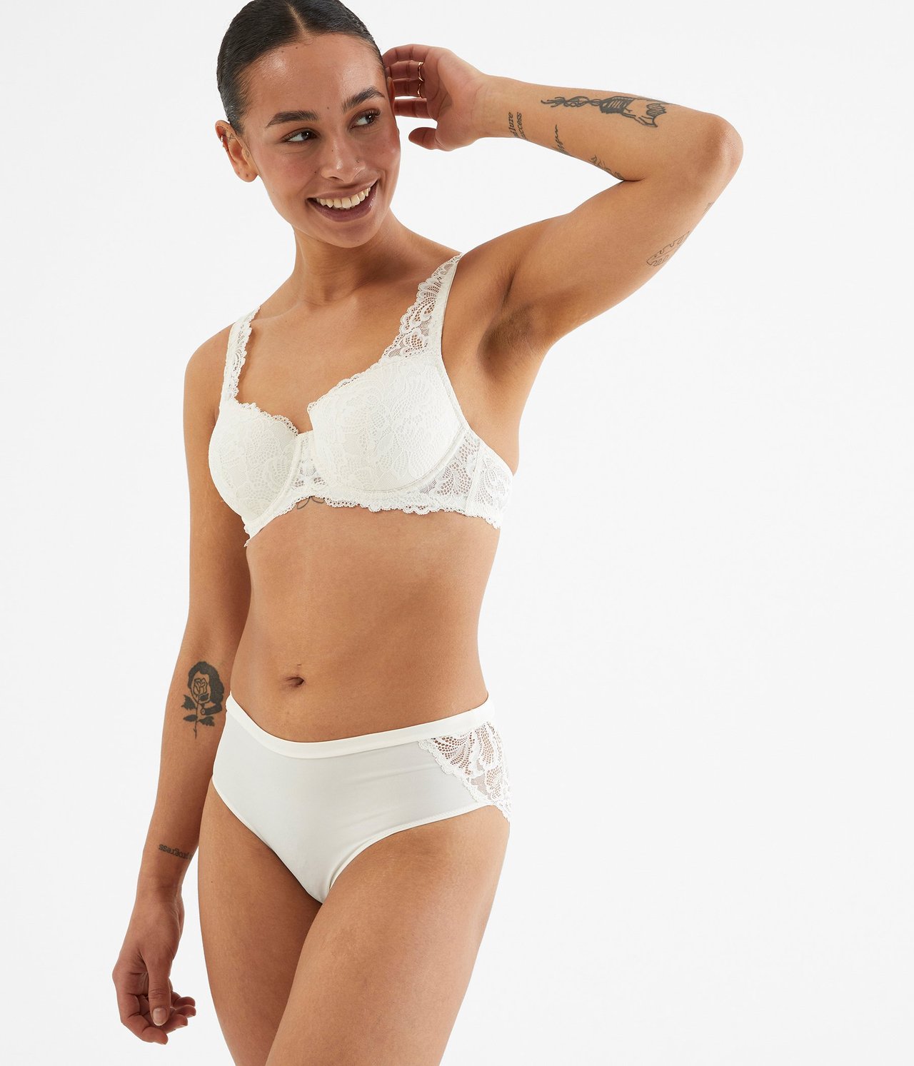 Forfra, kvinne i hvit blonde-BH og matchende hvite mikrotruser med blonder.