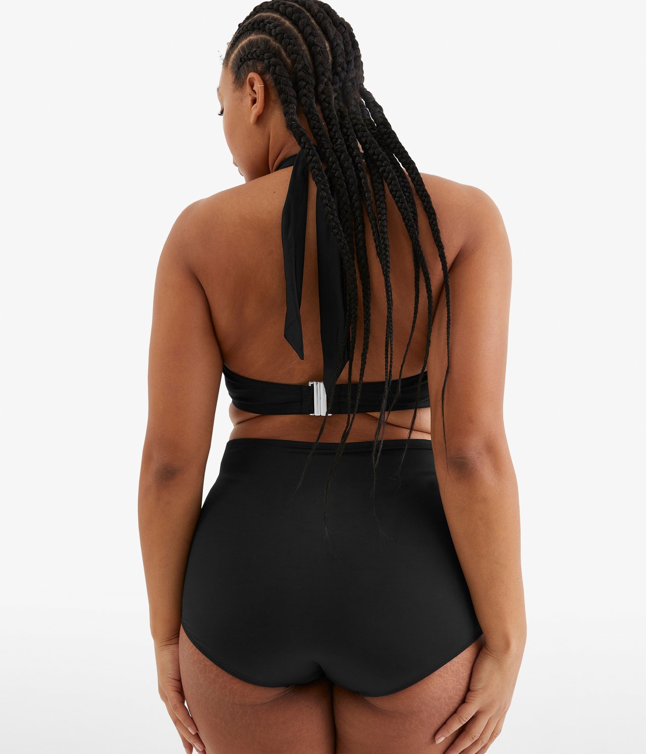 Bakifrån, kvinna i svarta högmidjade bikinitrosor och svart halterneck bikinitopp med silverspänne.
