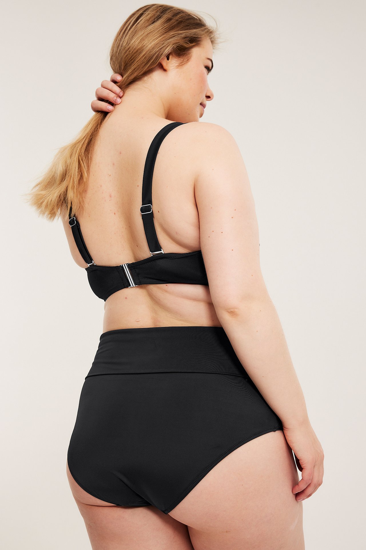 Kvinne bakfra i svart bikinitruse med foldbar midje og matchende svart bikinitopp.