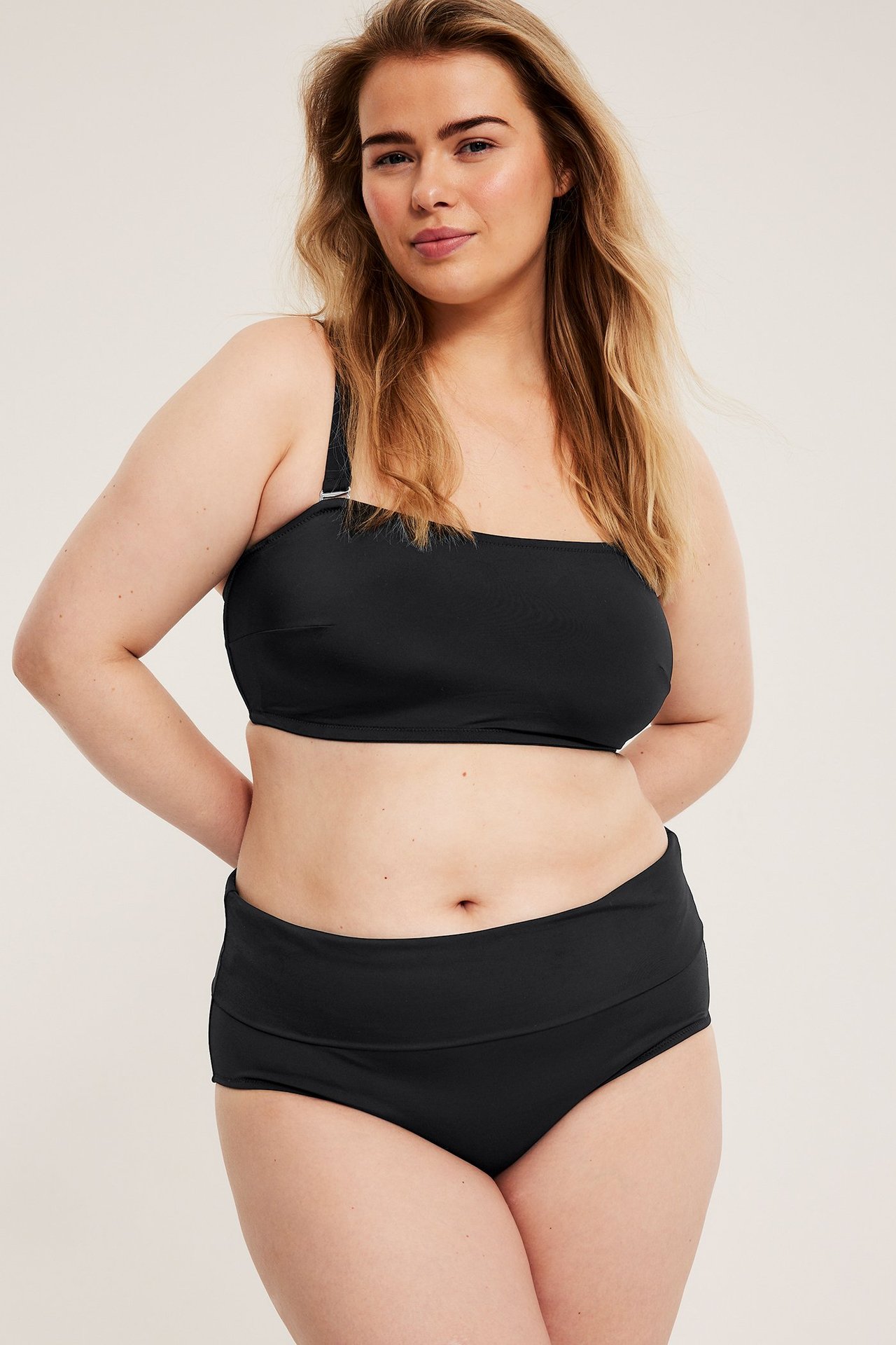 Frontutsikt, kvinne i svarte bikinitruser med vikbar midje og matchende bandeau-bikinitopp.