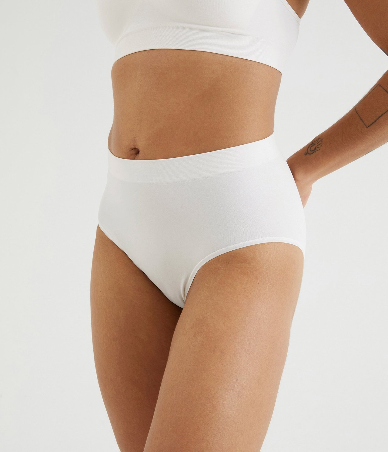 Sidovy av en kvinna i vita sömlösa höga trosor och matchande vit sömlös BH.